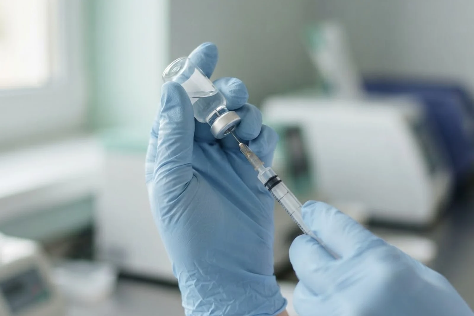 Gloved hands drawing a dose from a glass vial